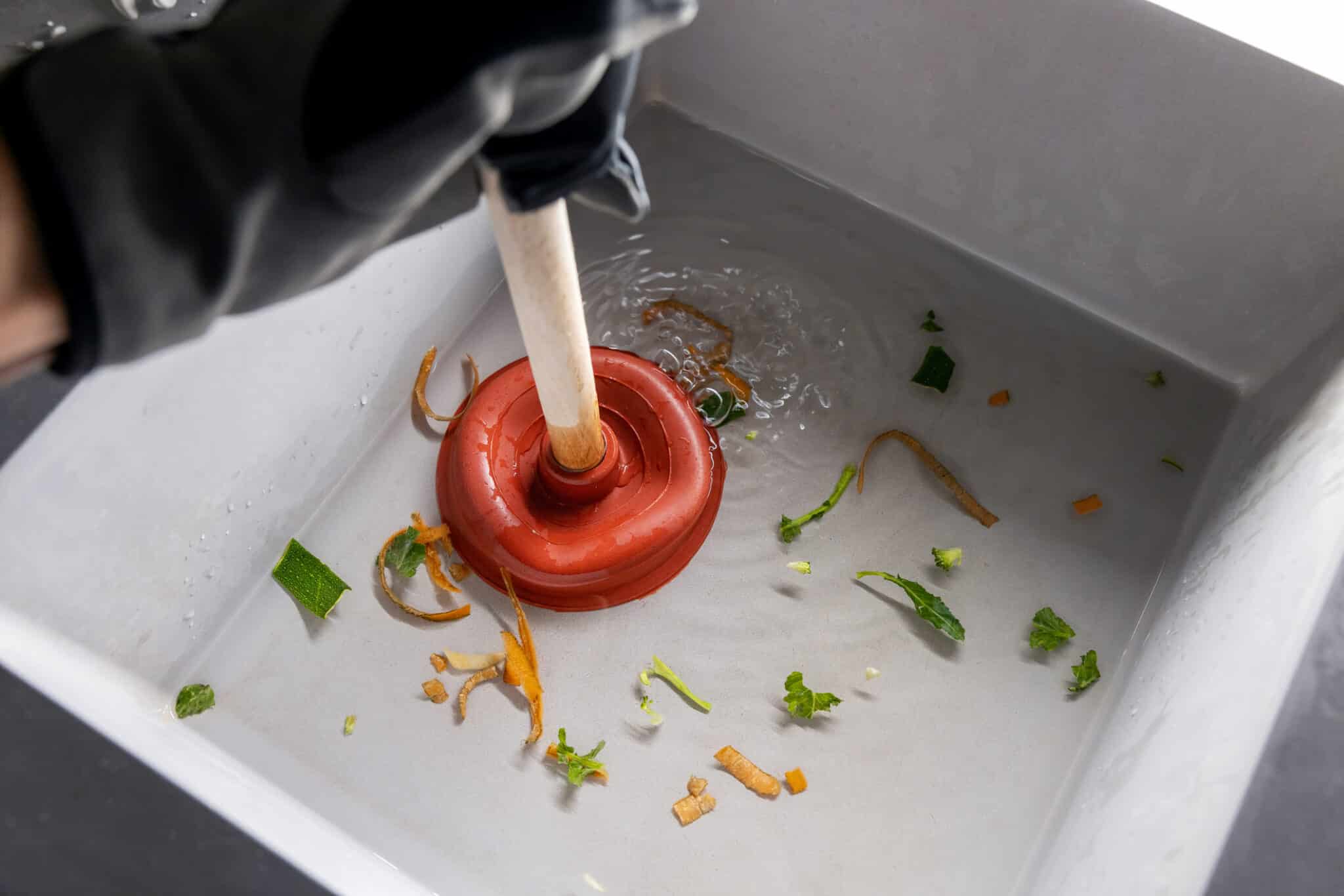 Plumbing cleans clogged kitchen sink with plunger.